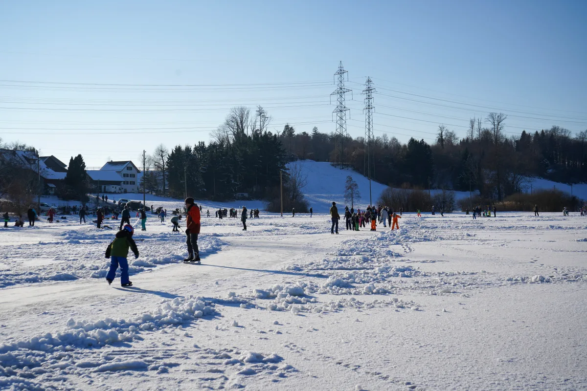 Man sieht Menschen auf einem gefrorenen Weiher. 